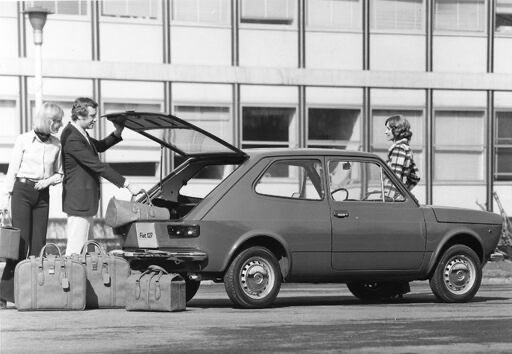 Fiat 127 auto takaluukku auki ja henkilö lastaamassa takaluukkuun tavaroita.