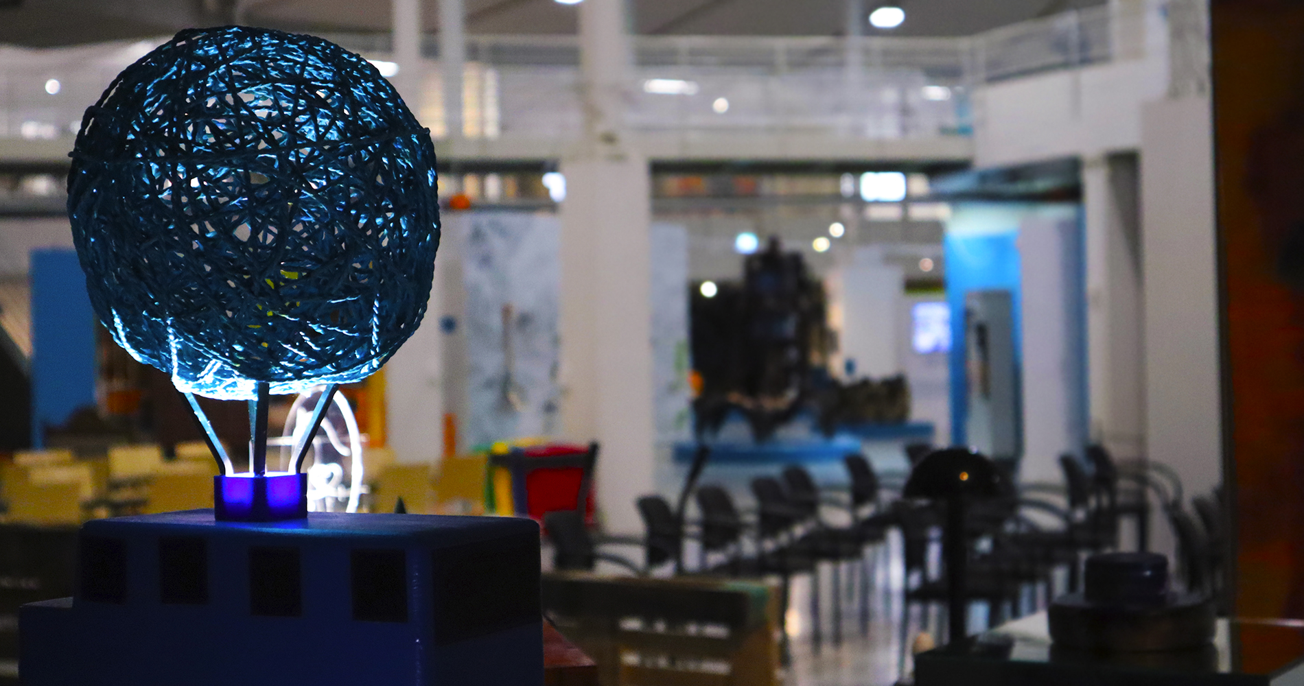 Kuva koululaisten valaisimia esitelleestä yhteisönäyttelystä, jossa vasemmalla yksi näyttelyn teoksista ja taustalla sumeana Tekniikan museo