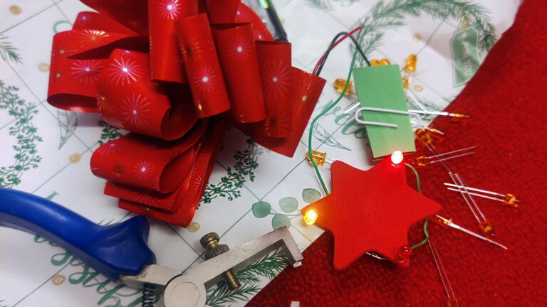 Tekniikan museon jouluvalotyöpajassa rakennettuja jouluvaloja ja niiden tekemiseen käytettyjä työvälineitä sekä punainen joulurusetti