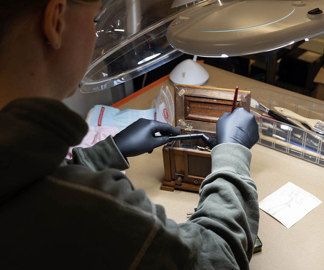 Kokoelmatyön amanuenssi kokoelmaesineen kanssa