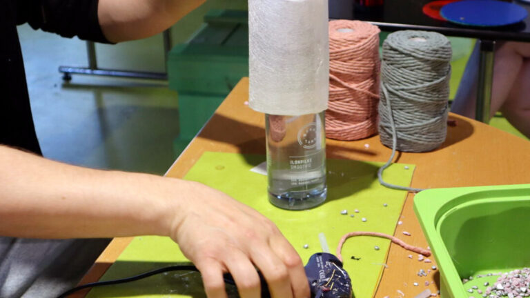 Korjaustorstaina pöydälle levitettyjä korjausmateriaaleja sekä kuumaliimapistooli, ihmisen kädet pitelevät niitä.